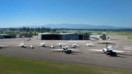 Multiple aircraft parked on ramp at Glacier Park International Airport with hangars and mountains