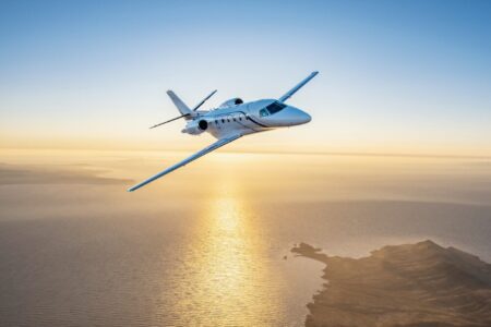 Cessna Citation Ascend midsize business jet flying over coastal waters during sunset