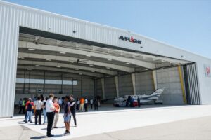 Guests gather outside the new Avflight hangar at Coleman A. Young International Airport during the facility opening, with a business jet visible inside the open hangar bay